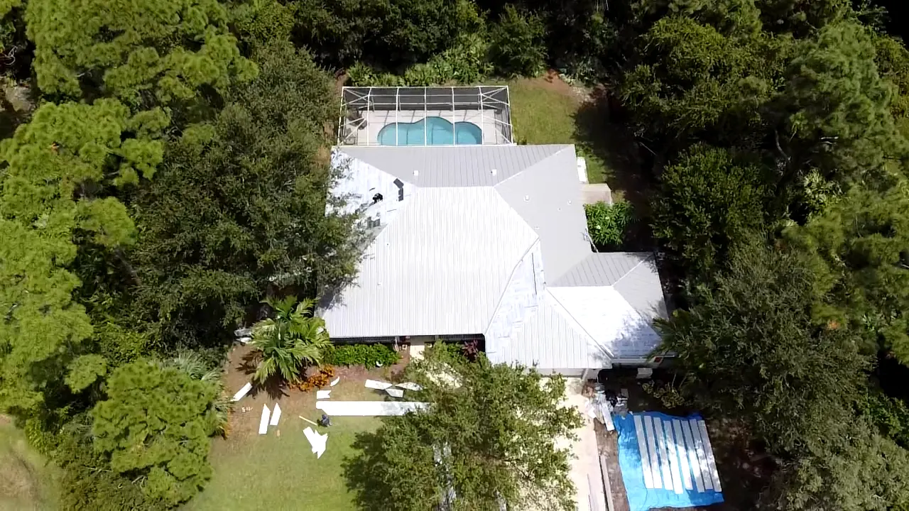 Aerial view of a completed white metal roof on a home with a pool