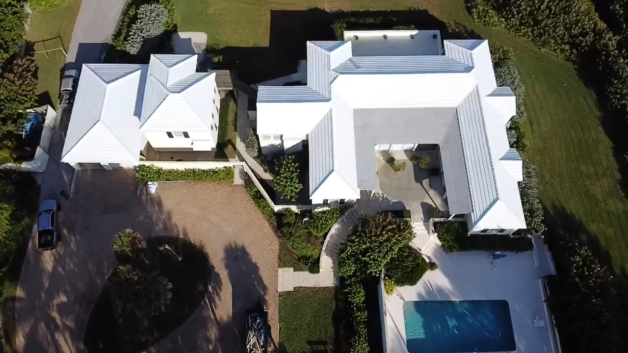 Aerial view of a waterfront home with a completed white metal roof