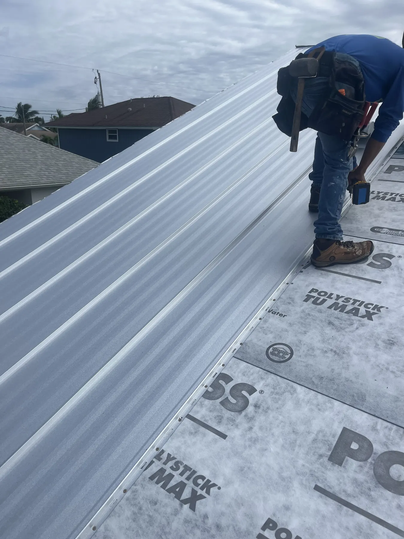 M&M roofing worker fastening a white metal panel over underlayment
